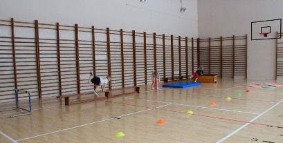 Dzieci z przedszkola ćwiczą na sali gimnastycznej - skok zawrotny przez ławeczkę, skok przez skrzynię, slalom