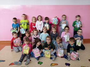 m 0dzieci z klasy 0 c, ustawione w trzech rzędach, trzymają w rękach prezenty i laurki dla babć i dziadków